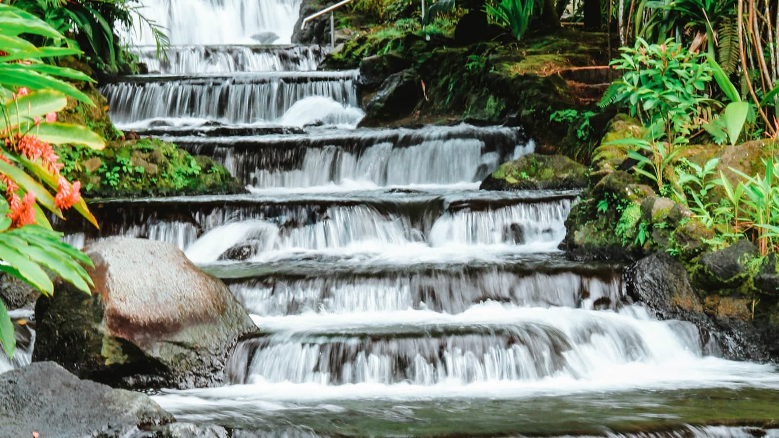 Cascading hot springs waterfall at a La Fortuna family resort, surrounded by tropical rainforest — the signature Arenal hotel experience